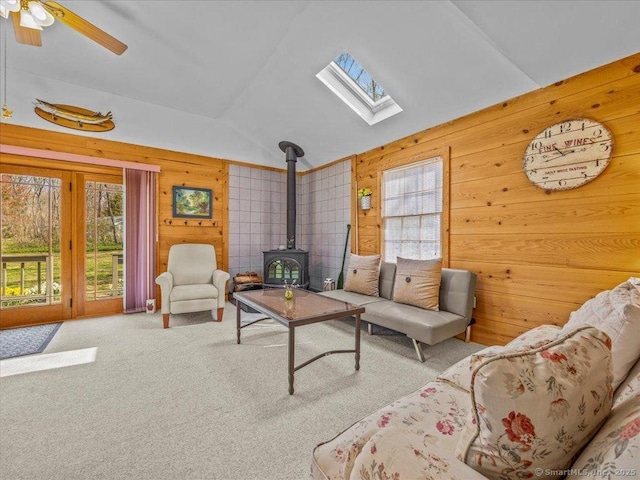 living room with wood walls, a wood stove, vaulted ceiling with skylight, and plenty of natural light