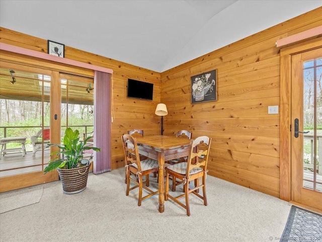 dining space with carpet, wood walls, and lofted ceiling
