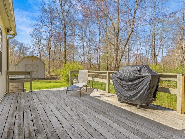 wooden terrace with a lawn, a storage unit, grilling area, and an outbuilding