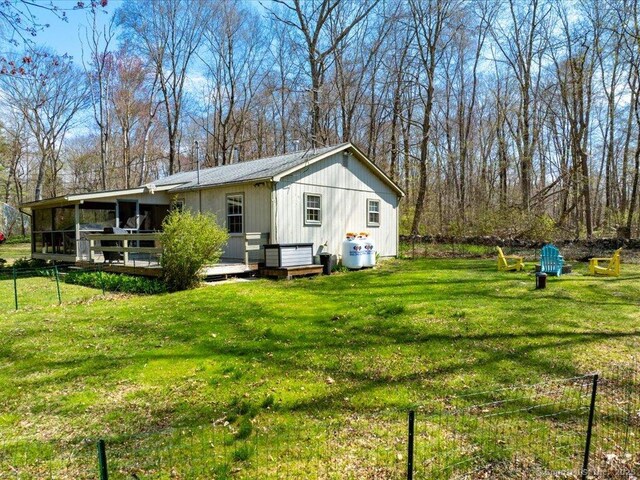 back of property with fence, a yard, a wooden deck, and a sunroom