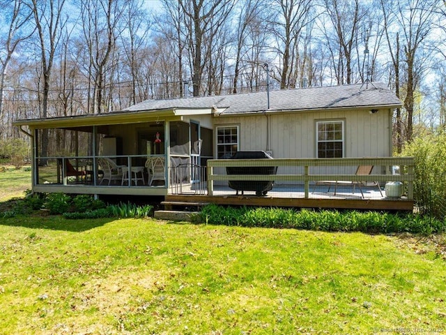 rear view of house with a deck, roof with shingles, a sunroom, and a lawn