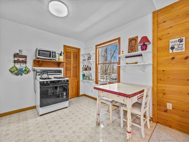 kitchen with stainless steel microwave, white range with gas stovetop, and baseboards
