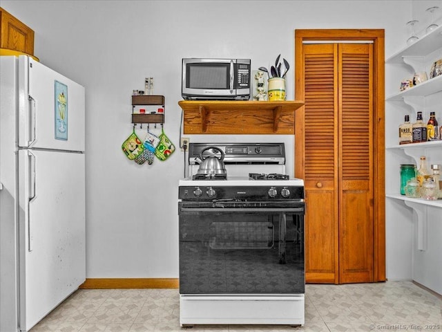 kitchen featuring freestanding refrigerator, stainless steel microwave, open shelves, gas stove, and baseboards