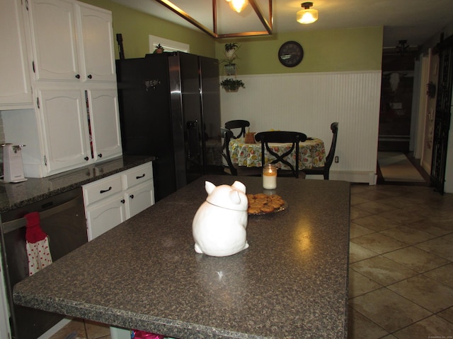 219 Forest St, East Hartford, CT 06118 - kitchen featuring black fridge with ice dispenser, dark countertops, white cabinetry, a wainscoted wall, and tile patterned flooring