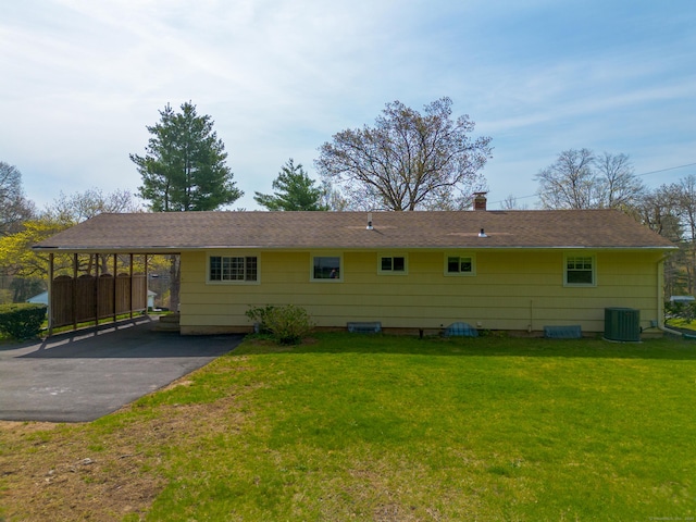 rear view of house featuring aphalt driveway, central AC unit, a chimney, a lawn, and a carport