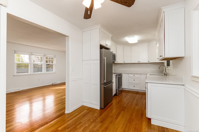 kitchen with ceiling fan, appliances with stainless steel finishes, a sink, light wood finished floors, and light countertops