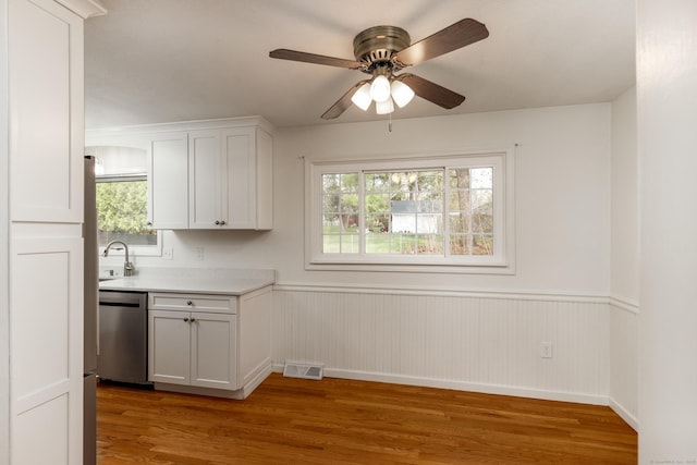 interior space featuring visible vents, stainless steel dishwasher, wainscoting, light countertops, and light wood finished floors