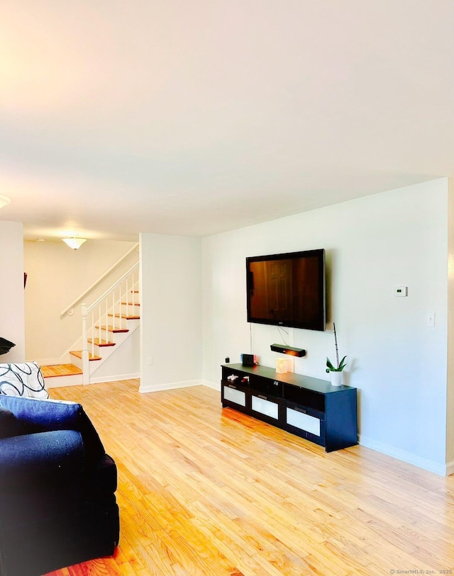 living room with stairs, light wood-type flooring, and baseboards