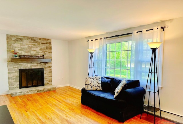 living room featuring wood finished floors, baseboard heating, baseboards, and a stone fireplace
