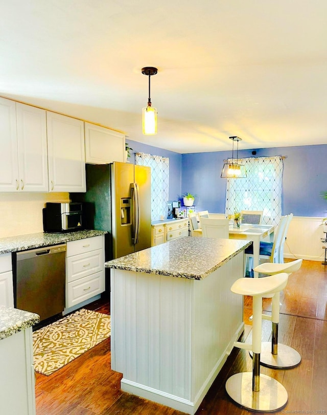 kitchen with stainless steel appliances, dark wood-type flooring, white cabinets, a center island, and light stone counters