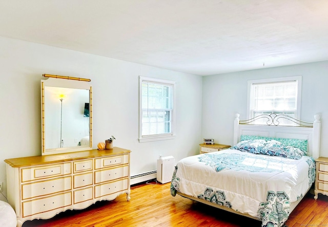 bedroom with baseboard heating, multiple windows, and wood finished floors