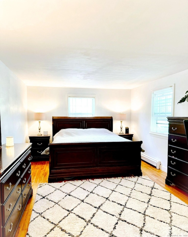 bedroom with a baseboard heating unit, light wood-type flooring, and baseboards