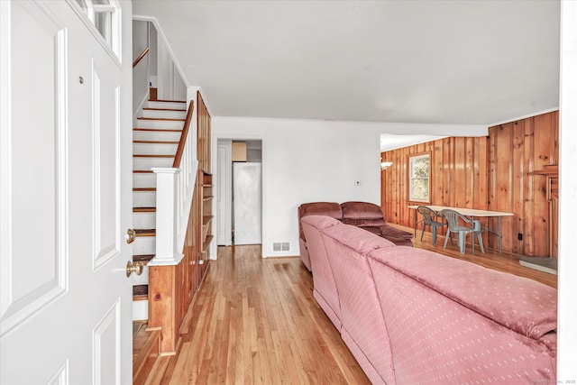 living room featuring stairway, light wood-style floors, wooden walls, visible vents, and baseboards