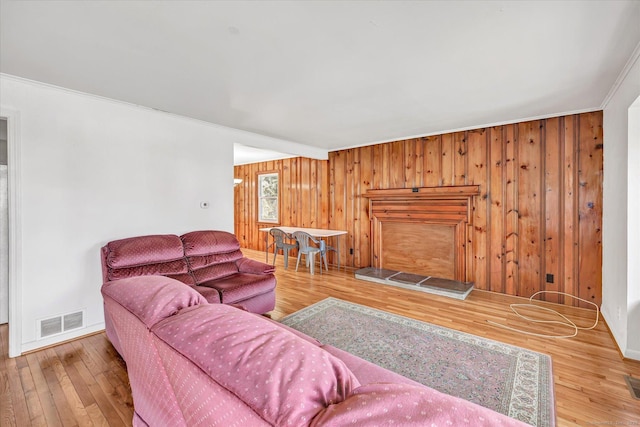 living room with crown molding, visible vents, wood walls, and hardwood / wood-style floors