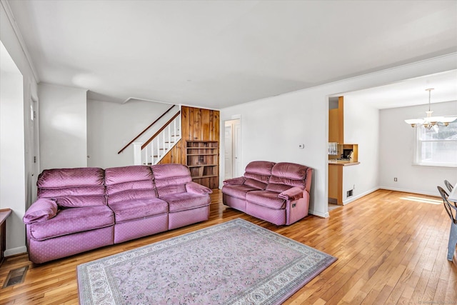 living area featuring stairway, light wood-style floors, baseboards, visible vents, and a notable chandelier