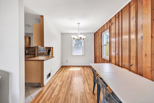 unfurnished dining area featuring an inviting chandelier, baseboards, and light wood-type flooring