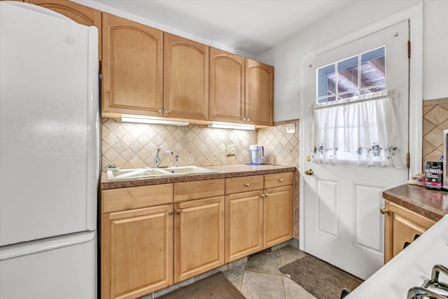 kitchen with light brown cabinetry, decorative backsplash, freestanding refrigerator, and a sink