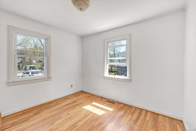 unfurnished room featuring baseboards, visible vents, wood finished floors, and plenty of natural light