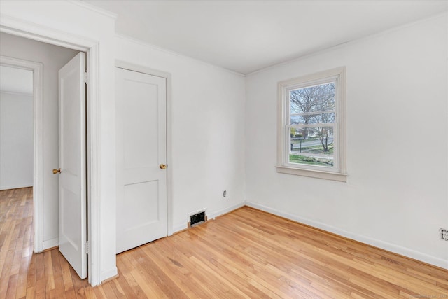 empty room with crown molding, visible vents, baseboards, and light wood-type flooring