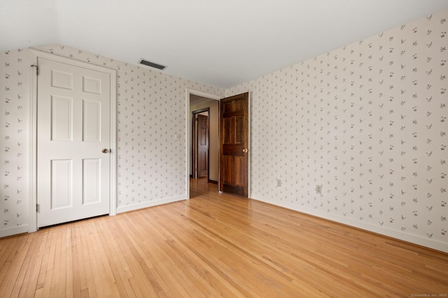 unfurnished room featuring visible vents, lofted ceiling, baseboards, wallpapered walls, and light wood finished floors