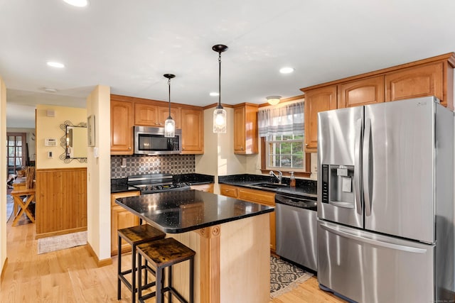 kitchen featuring stainless steel appliances, a sink, light wood-style floors, a center island, and a wainscoted wall