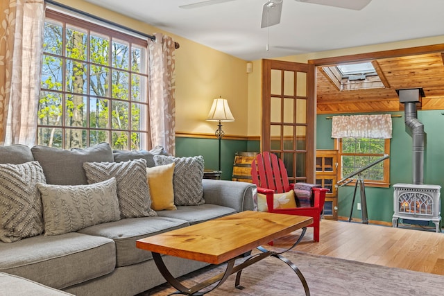 sitting room with a wood stove, a skylight, wood finished floors, and ceiling fan
