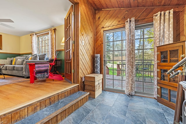 mudroom with stone tile floors, ceiling fan, and wooden walls