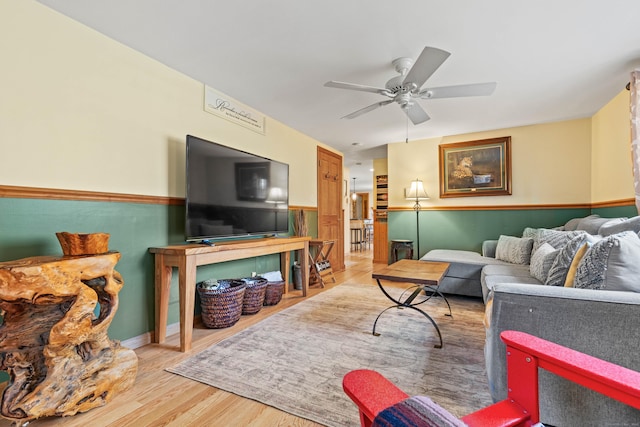 living room with wood finished floors, a ceiling fan, and wainscoting