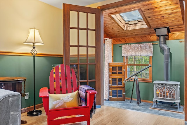 living area with a skylight, a wood stove, wood finished floors, baseboards, and vaulted ceiling