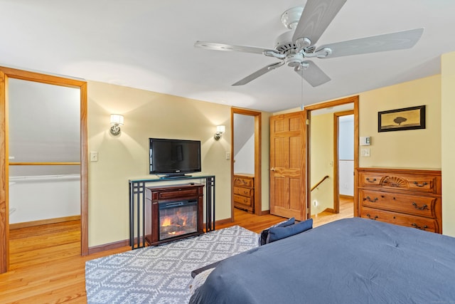 bedroom with light wood-style flooring, a glass covered fireplace, baseboards, and a ceiling fan