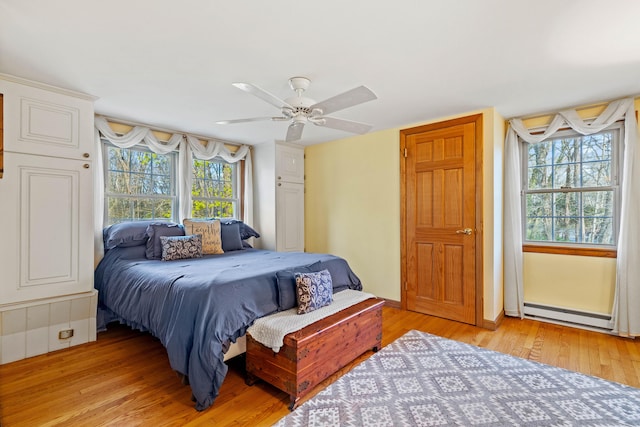 bedroom featuring light wood-type flooring, baseboard heating, and a ceiling fan