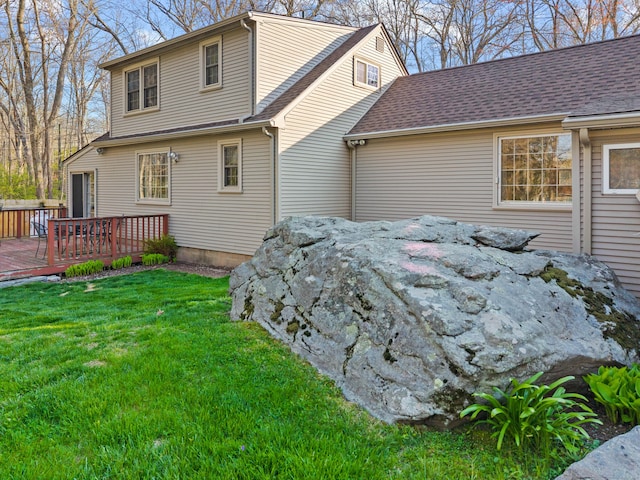 back of property with a wooden deck, a lawn, and roof with shingles