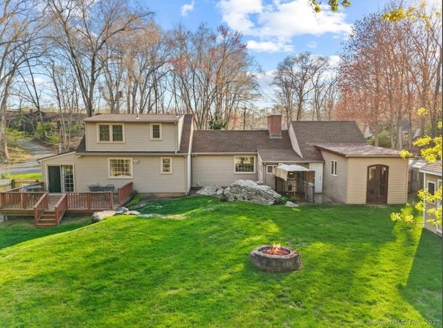 back of house featuring a fire pit, a wooden deck, a yard, and a chimney