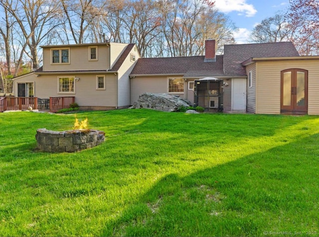 rear view of house featuring a fire pit, a chimney, a lawn, and a wooden deck