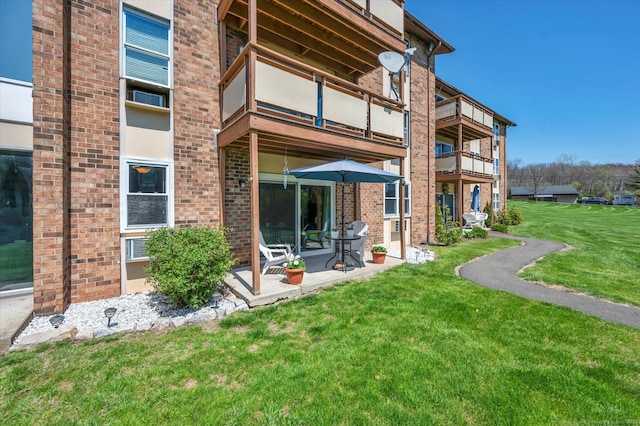 rear view of property with a patio, brick siding, a balcony, and a lawn