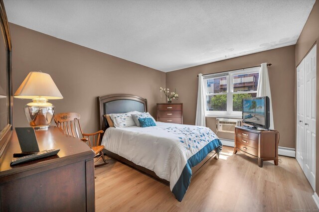 bedroom featuring baseboard heating, light wood-style floors, a closet, and a wall mounted AC