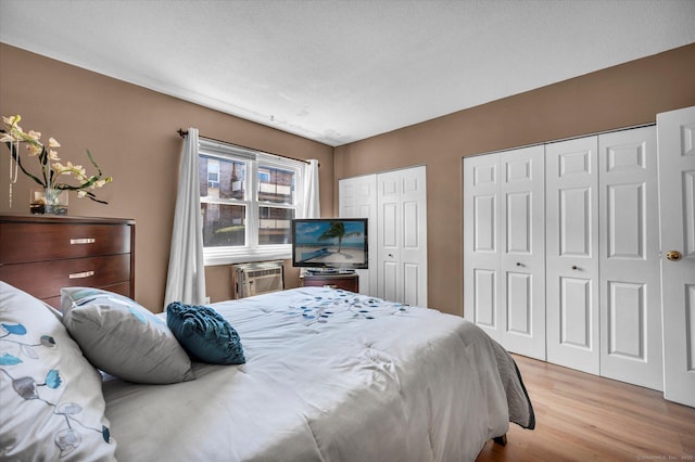 bedroom featuring a wall mounted air conditioner, wood finished floors, and two closets