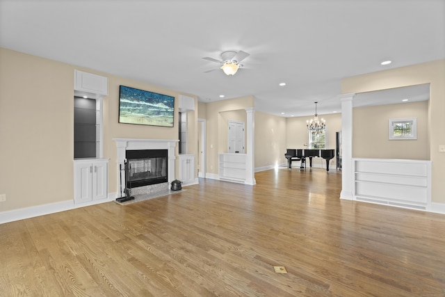 unfurnished living room with light wood finished floors, a glass covered fireplace, ceiling fan with notable chandelier, recessed lighting, and ornate columns