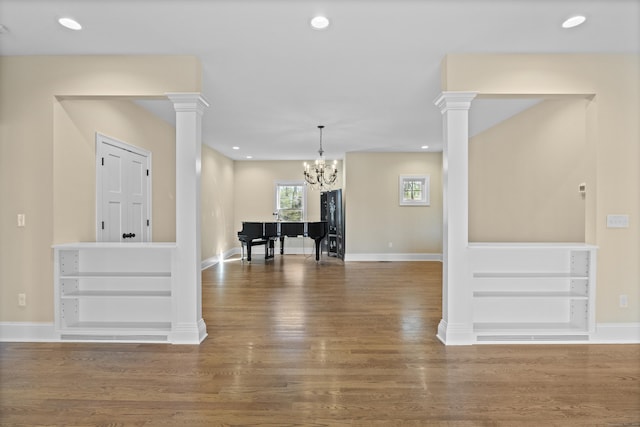 interior space featuring ornate columns, baseboards, wood finished floors, and a notable chandelier