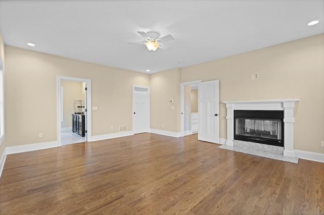 unfurnished living room with visible vents, wood finished floors, baseboards, ceiling fan, and a multi sided fireplace