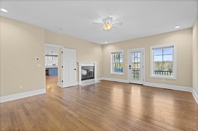 unfurnished living room with visible vents, wood finished floors, baseboards, a high end fireplace, and a ceiling fan