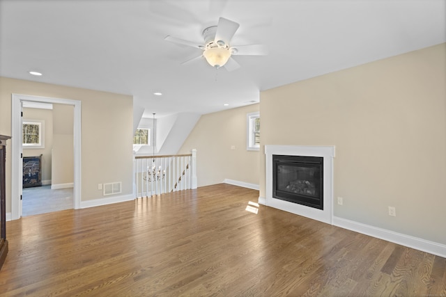 unfurnished living room featuring a glass covered fireplace, a ceiling fan, baseboards, wood finished floors, and visible vents