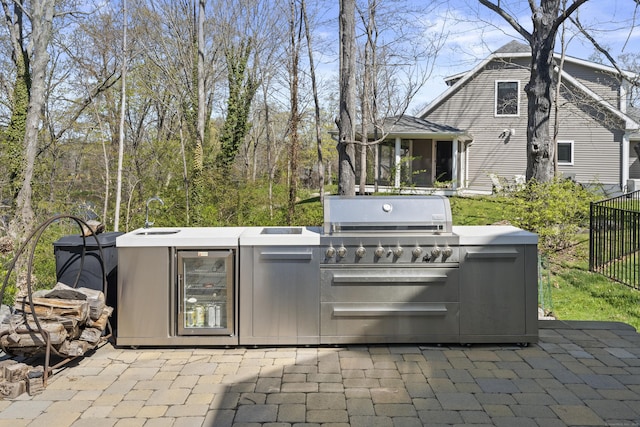view of patio featuring fence, wine cooler, an outdoor kitchen, a sunroom, and a sink