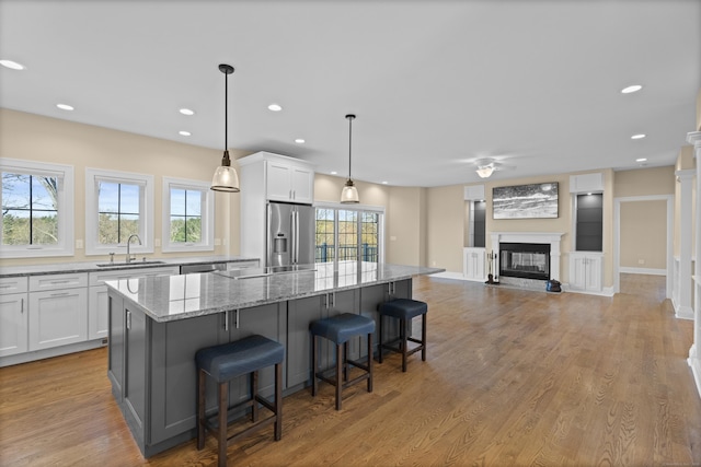 kitchen with appliances with stainless steel finishes, a center island, light stone countertops, a sink, and white cabinets