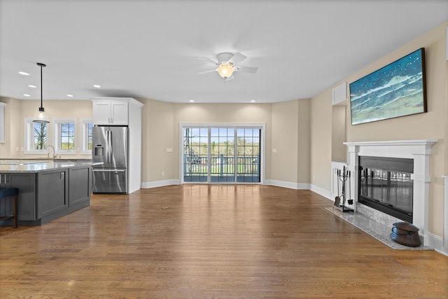 unfurnished living room with a healthy amount of sunlight, a ceiling fan, a fireplace with flush hearth, a sink, and dark wood-style floors
