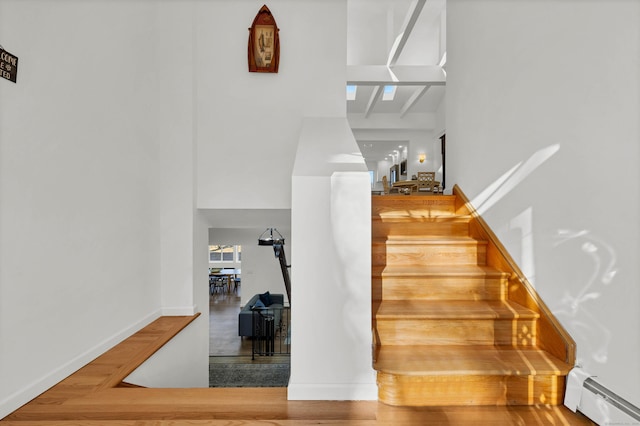 stairs featuring a baseboard radiator, a towering ceiling, wood finished floors, and baseboards