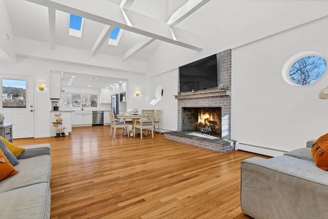 living area featuring a baseboard radiator, light wood-style floors, lofted ceiling with skylight, and a brick fireplace