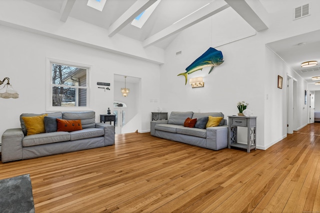 living area featuring beam ceiling, light wood-type flooring, visible vents, a skylight, and high vaulted ceiling