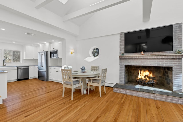 dining space with baseboard heating, light wood-style flooring, vaulted ceiling with beams, a fireplace, and visible vents