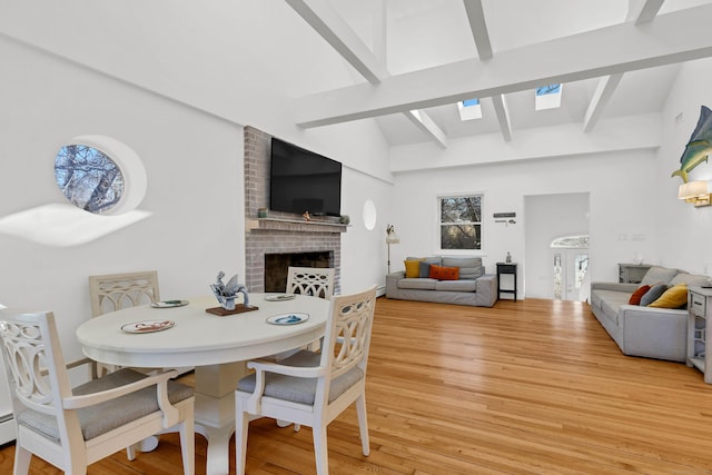 dining space featuring vaulted ceiling with skylight, light wood finished floors, and a fireplace